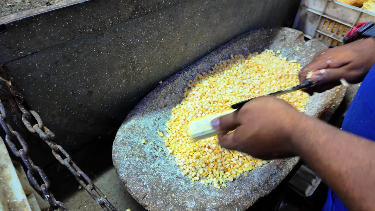 A dark-skinned man's hands cutting corn cobs.Close up downward view