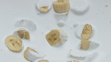 creamy fresh banana yogurt with sweet pieces dropped on white surface close up.