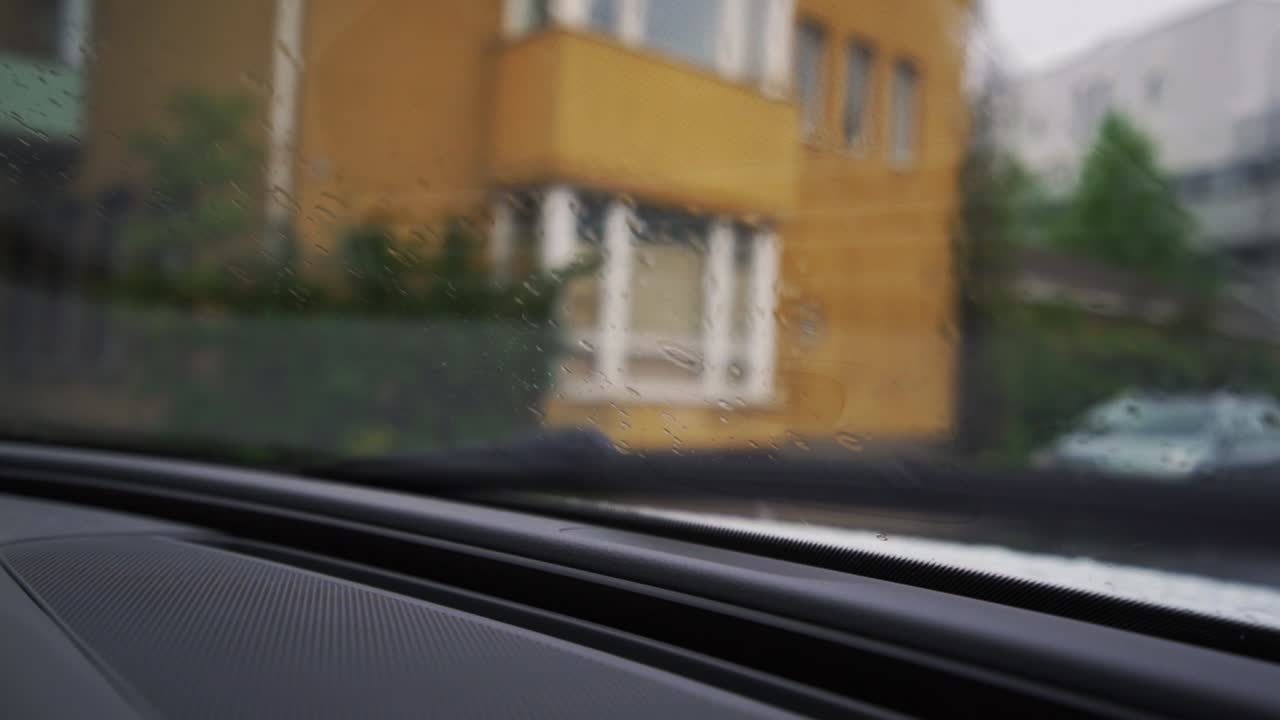 Windshield wipers wipe rain off of a car driving down the street on rainy day