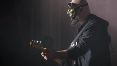 a man in a mask plays an electric bass guitar at a rock concert in a club. nightlife in a big city. red and blue lighting