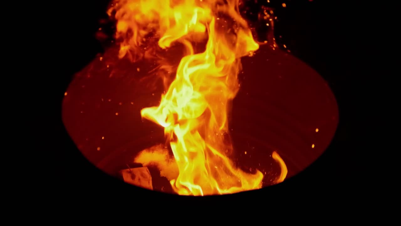 Cinematische 4K close-up van een hand die 's nachts een stuk hout in een knapperend kampvuur plaatst.