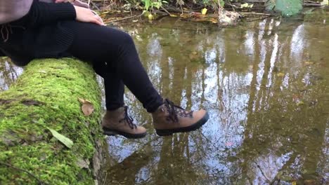 a woman sitting on a log laying over the small stream