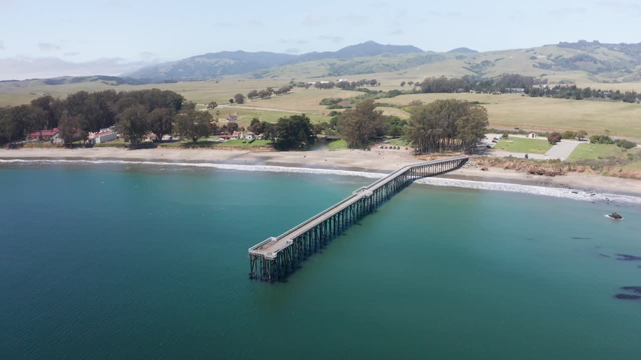 Descending and panning aerial shot of the William Randolph Hearst Memorial Beach Pier in Old San Simeon Village on the Central Coast of California