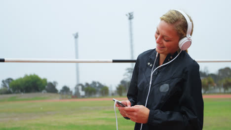 front view of caucasian female athlete listening music on mobile phone at sports venue 4k