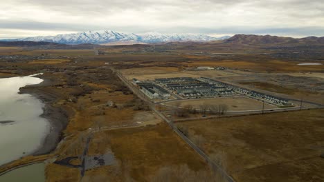flying high over a lake shoreline towards the mountains and new suburban development in saratoga springs, utah
