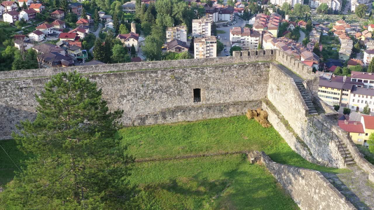 Slow aerial backward drone view above lush green grass on rooftop of Pocitelj castle