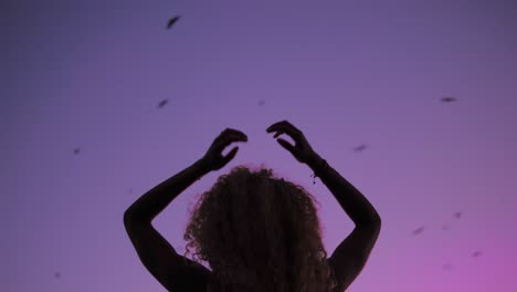 silhouette of a gorgeous lady dancing gracefully under the purple sky during sunset with bats flying - close-up shot