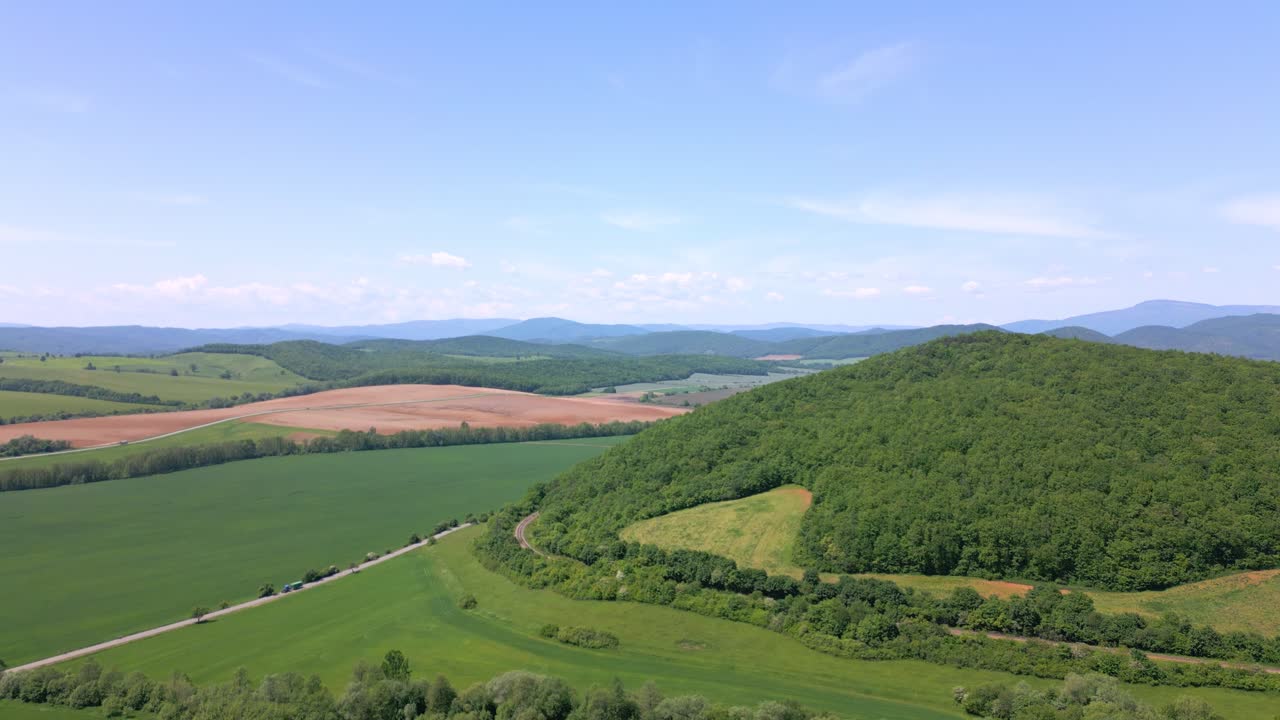 Grønne marker og jordbruksområder i middagssolen, dronefotografert med et kupert landskap i bakgrunnen.