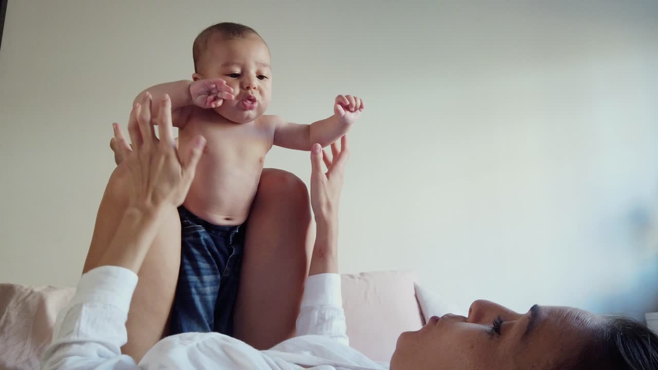 Madre feliz sin rostro jugando con su bebé en el dormitorio