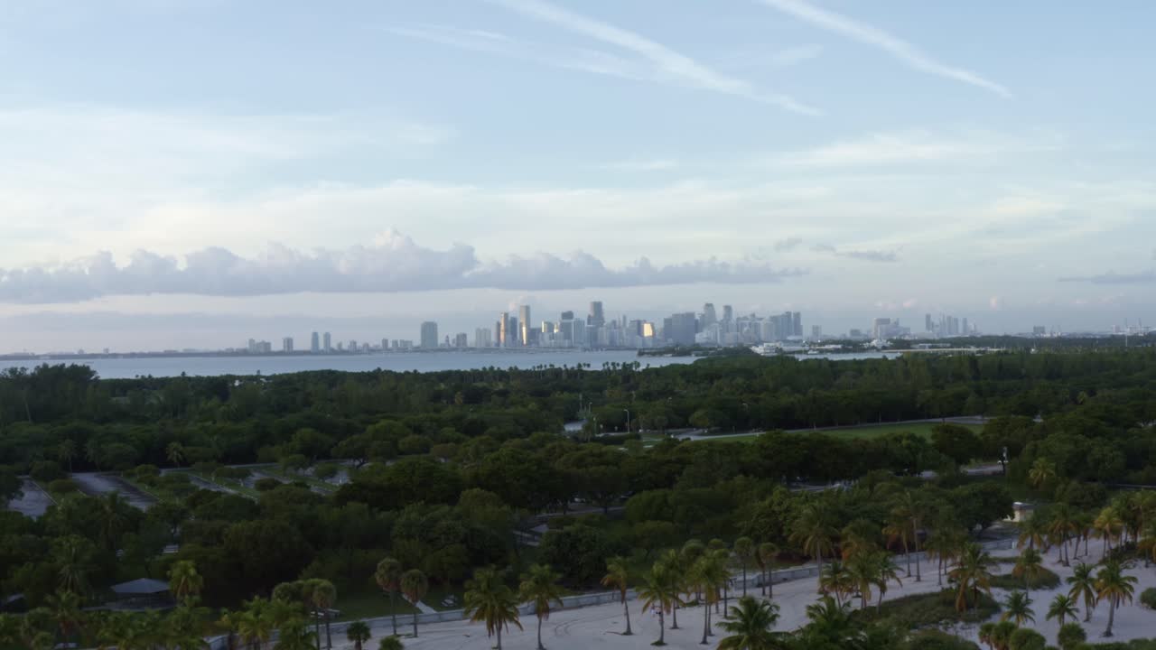 tomada aérea de la playa tropical rodeada de palmeras en el parque crandon en key biscayne con el horizonte de miami, florida en la distancia en una soleada noche de verano