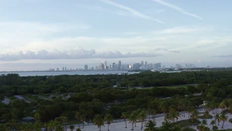 dolly out aerial drone shot of the tropical beach surrounded by palm trees on crandon park in key biscayne with the skyline of miami, florida in the distance on a sunny summer evening