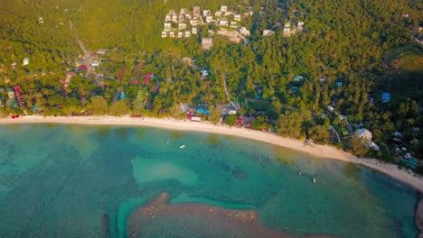 un dron aéreo de 4k empuja la toma de la playa de ensalada en koh phangan en tailandia con barcos de pesca, agua verde azulado, coral y selvas verdes