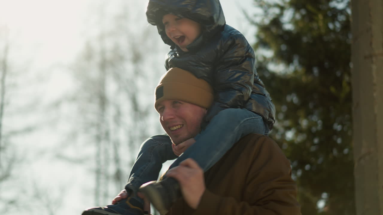 Close up of father playing with his son leg on his shoulder as the child is excited with trees in the background