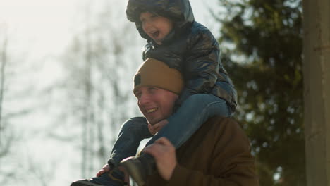 close up of father playing with his son leg on his shoulder as the child is excited with trees in the background