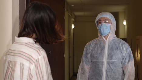 man in a protective suit holding a sign that says "let's stop coronavirus" talking to a woman in a hallway.