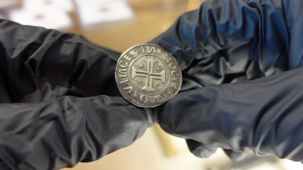 coleccionista examinando una moneda de plata portuguesa de la época medieval