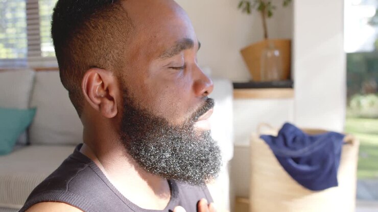 Uomo afroamericano concentrato che pratica meditazione yoga a casa, slow motion