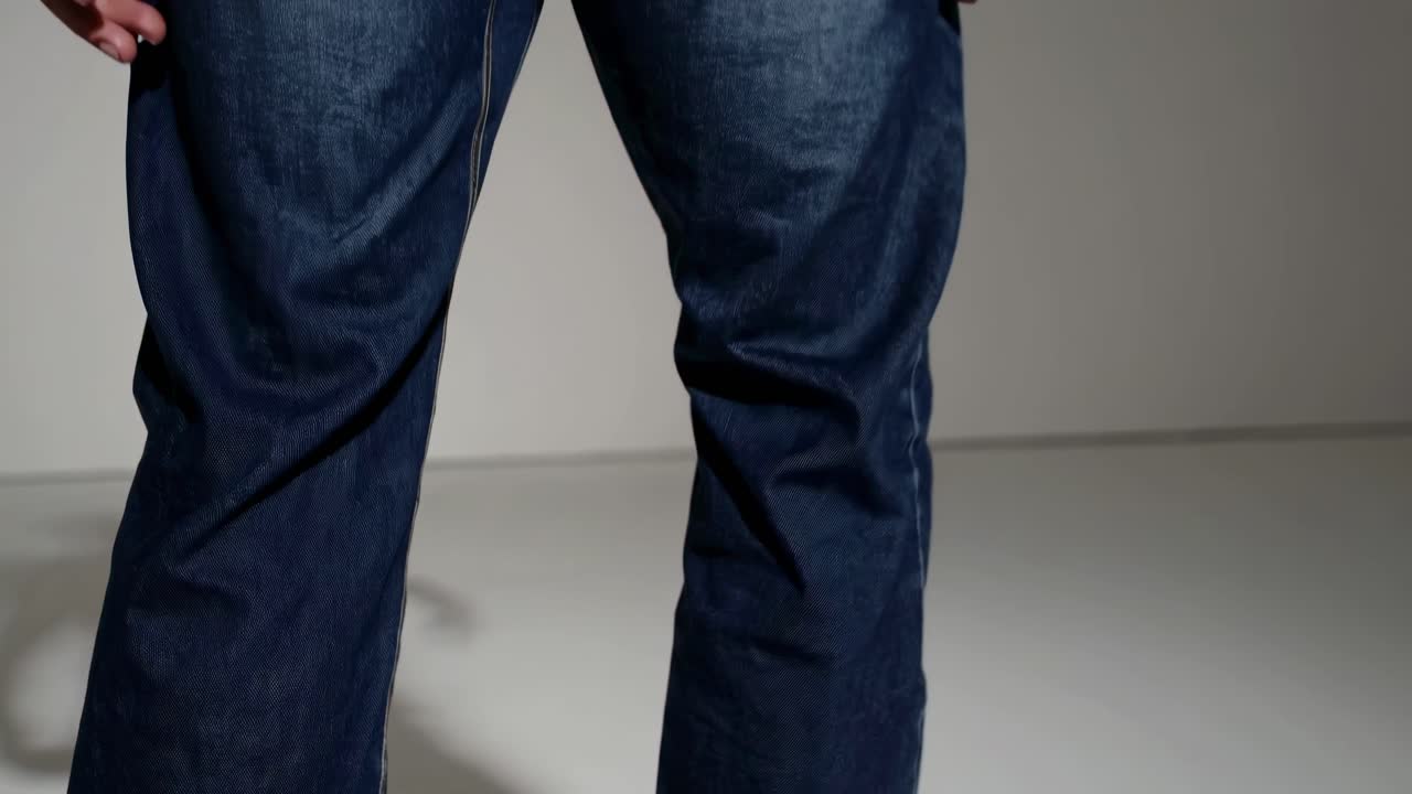 Close-up video of dark denim jeans from a low angle, highlighting texture and style in a minimalist