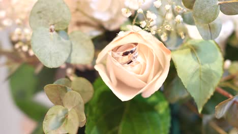 Panorama-bouquet-of-white-roses-with-wedding-rings-between-their-petals,-surrounded-by-eucalyptus-leaves-and-other-foliage