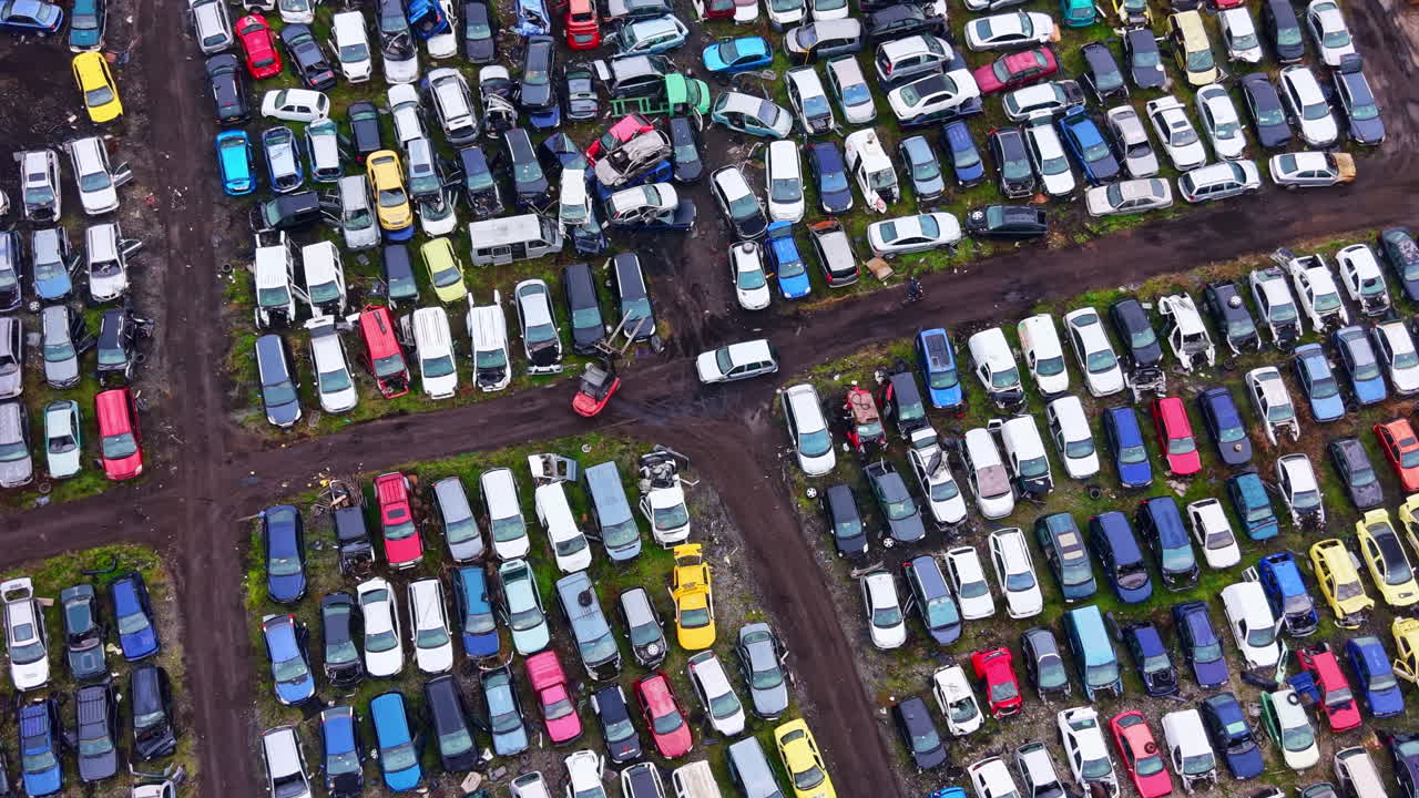 Vasta collezione di auto usate in uno sfasciacarrozze situato in un'area rurale, che mostrano vari colori e condizioni di giorno.