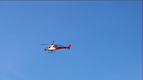 a red helicopter flies smoothly across a bright blue sky in queenstown, new zealand, showcasing dynamic aerial movement and serene atmosphere