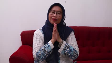 Happy-excited-asian-elderly-woman-greeting-to-the-camera-while-siiting-on-the-sofa-at-home