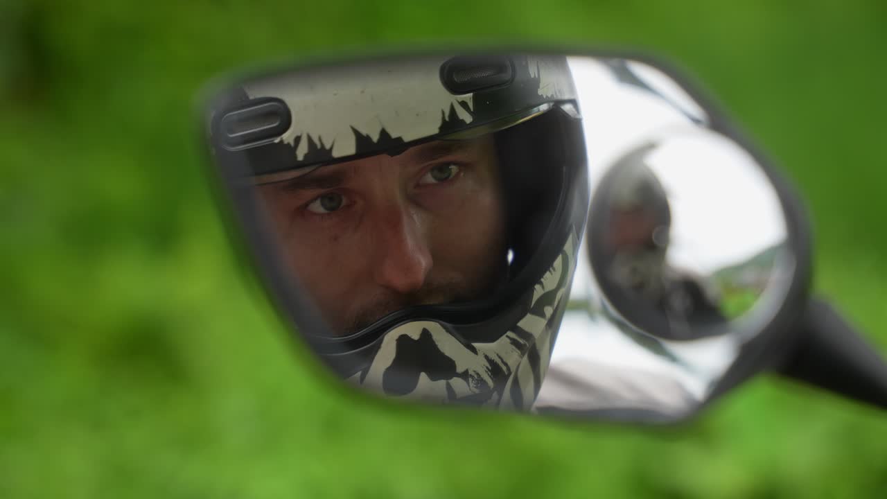A close‑up reflection shot in a motorcycle side mirror of helmeted rider, eyes visible through visor, putting it down with the green outdoor blurs behind in Mahabang Tanaw, Quezon Province Philippines