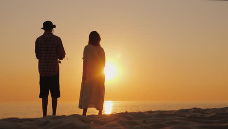 a man is fishing on the beach his pregnant wife is standing nearby