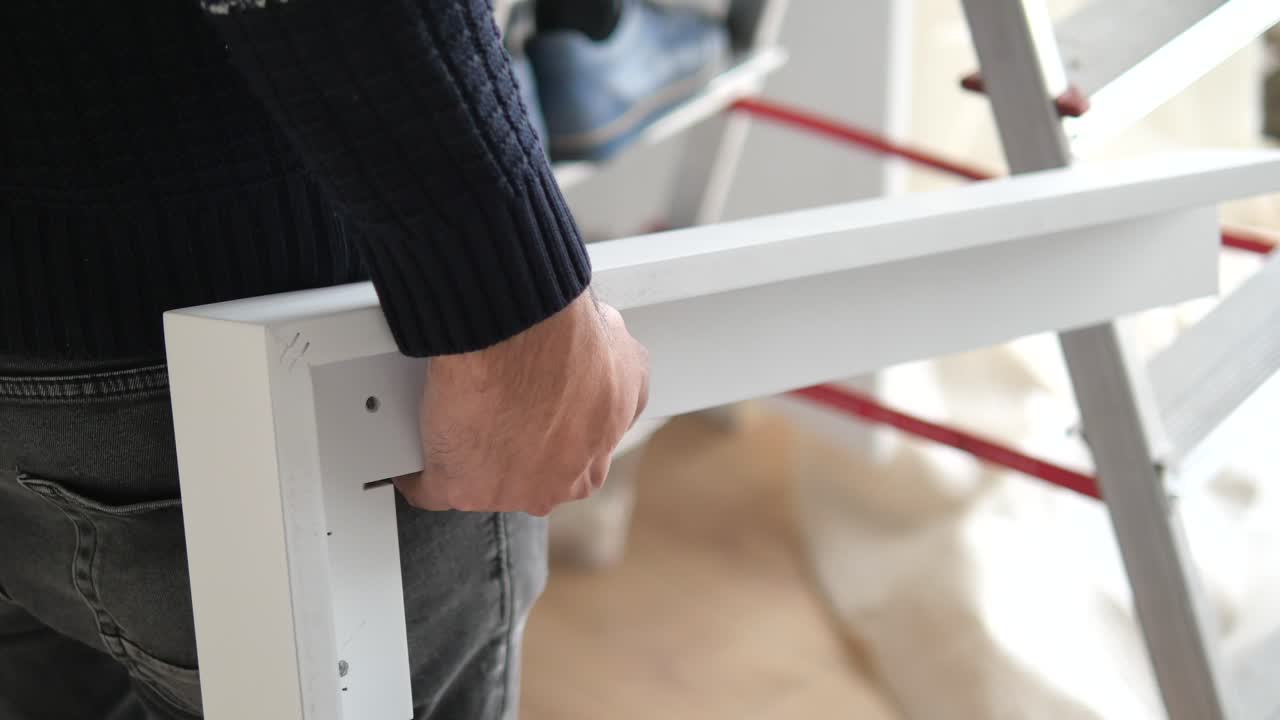 Uomo che tiene in mano una cornice di legno bianca, forse per una foto o una mensola, mentre lavora a un progetto di miglioramento domestico