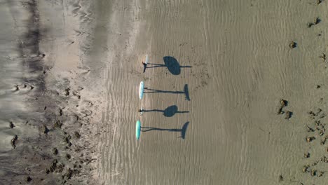 Friends-walking-on-beach-with-surfboards-casting-shadows