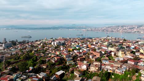 aerial dolly in of playa ancha hill neighborhood houses near sea port, container cargo ships in background, valparaíso, chile