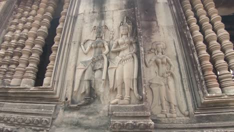 Slow-pan-around-the-detailed-facade-of-a-temple-gallery-in-Angkor-Wat,-Cambodia,-picturing-three-women