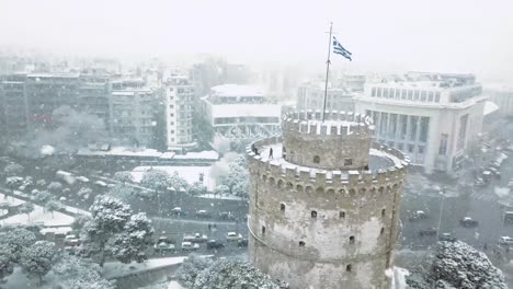 Imágenes-Aéreas-De-La-Torre-Blanca-De-Tesalónica-Durante-La-Tormenta-De-Nieve,-Bandera-Griega-Ondeando-En-La-Parte-Superior-Del-Castillo