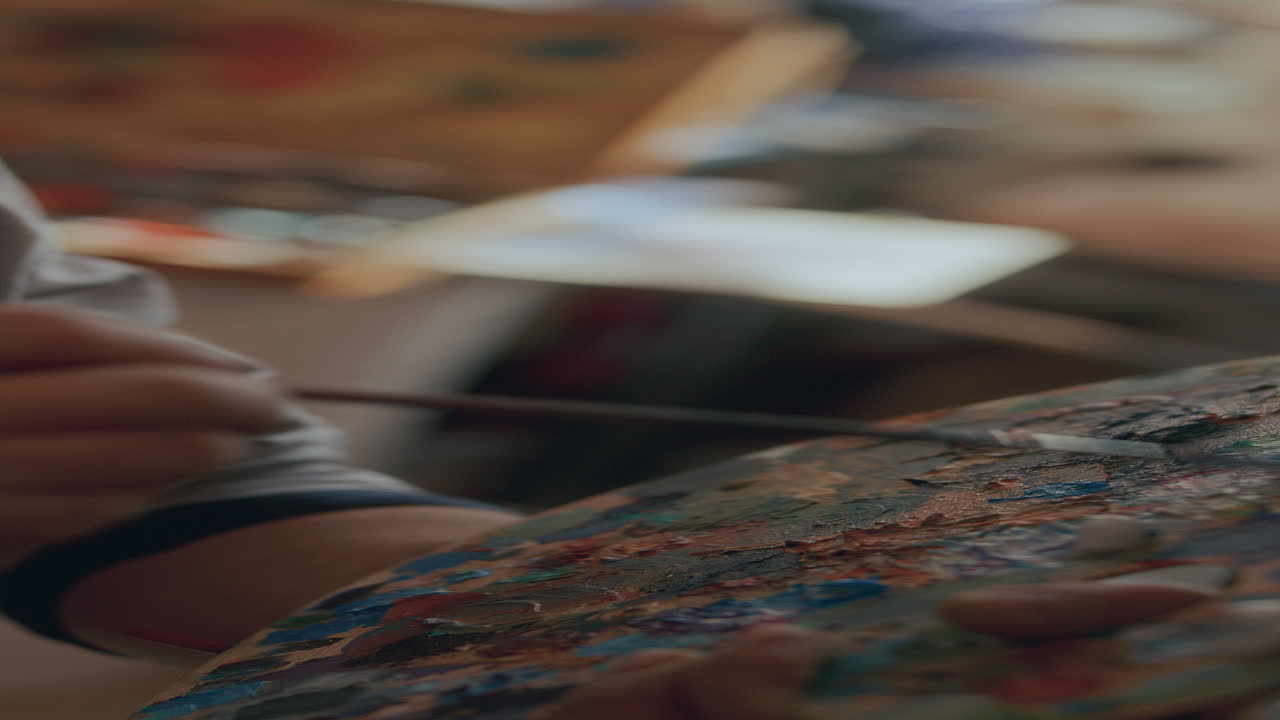パレットで筆を使って絵の具を混ぜるアーティストの手のクローズアップ