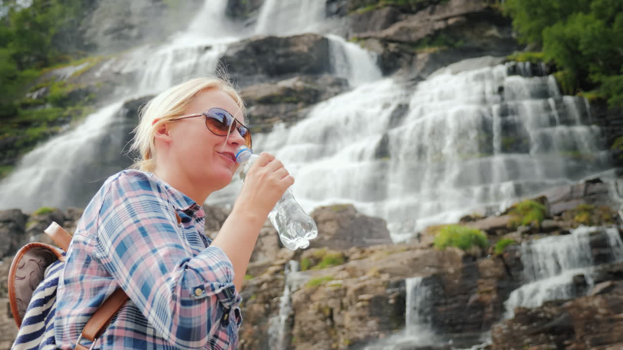 젊은 여성은 노르웨이 깨끗한 drinki에서 트윈 폭포 tvindefossen의 배경에 물을 마신다