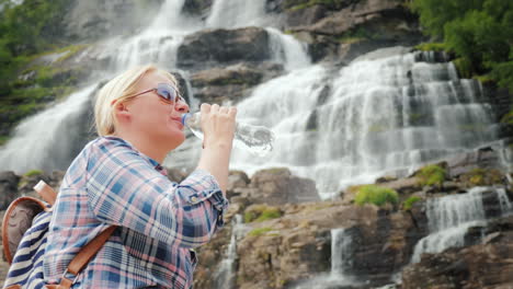 young woman drinks water on the background of the twin waterfall tvindefossen in norway clean drinki