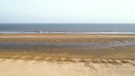 Male-sat-on-sand-dunes-looking-out-across-the-sea-with-the-tide-out-early-morning-in-Holme-next-the-Sea,-Norfolk,-England