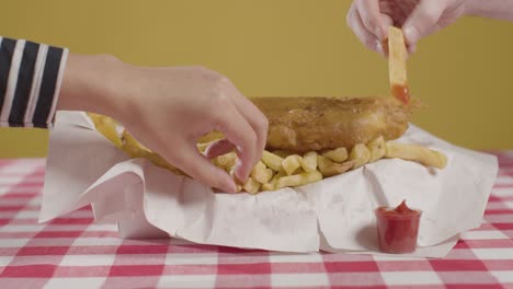 people using fingers to eat traditional british takeaway meal of fish and chips with ketchup