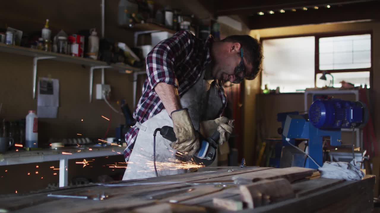 Caucasian male knife maker in workshop wearing glasses and using angle grinder