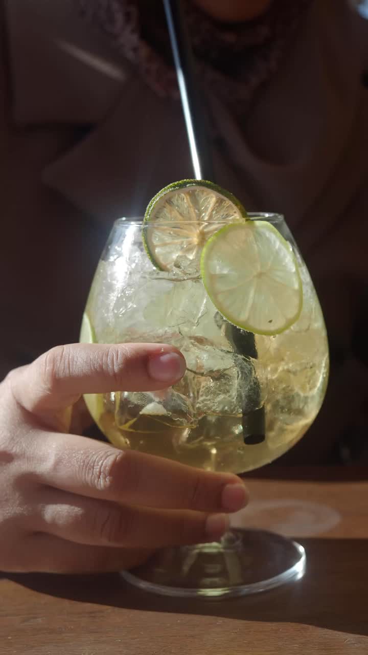 Primo piano di una mano che tiene un cocktail rinfrescante con lime e ghiaccio