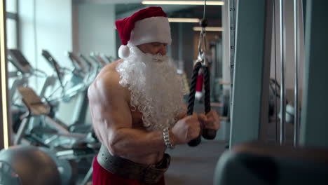 papá noel deportivo haciendo extensión de cuerda en el gimnasio. hombre en forma entrenando en club deportivo