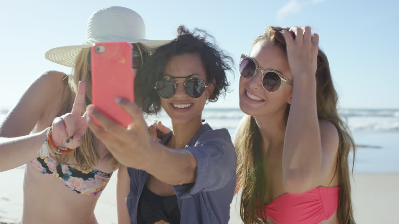 Gruppo di amiche che si scattano selfie in spiaggia usando un telefono rosa