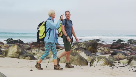 Senior-hiker-couple-with-backpack-and-hiking-poles-talking-to-each-other-and-walking-while-hiking