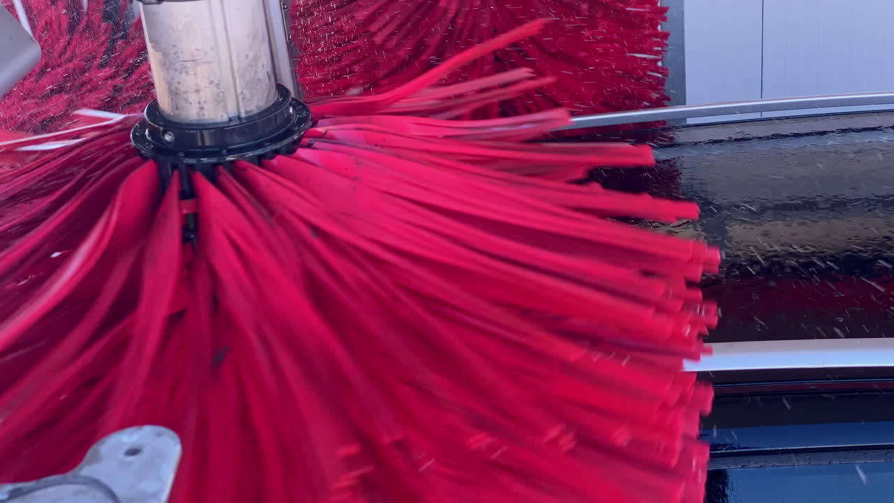 Rotating red brush cleaning a car's black roof inside an automatic car wash, showcasing modern vehicle maintenance and service