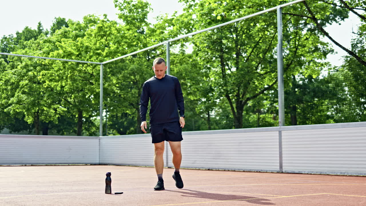 Athletic man in shorts and jersey doing sports outdoors. Guy doing exercises on a sports ground in a city park. Healthy lifestyle. Sport in a man's life