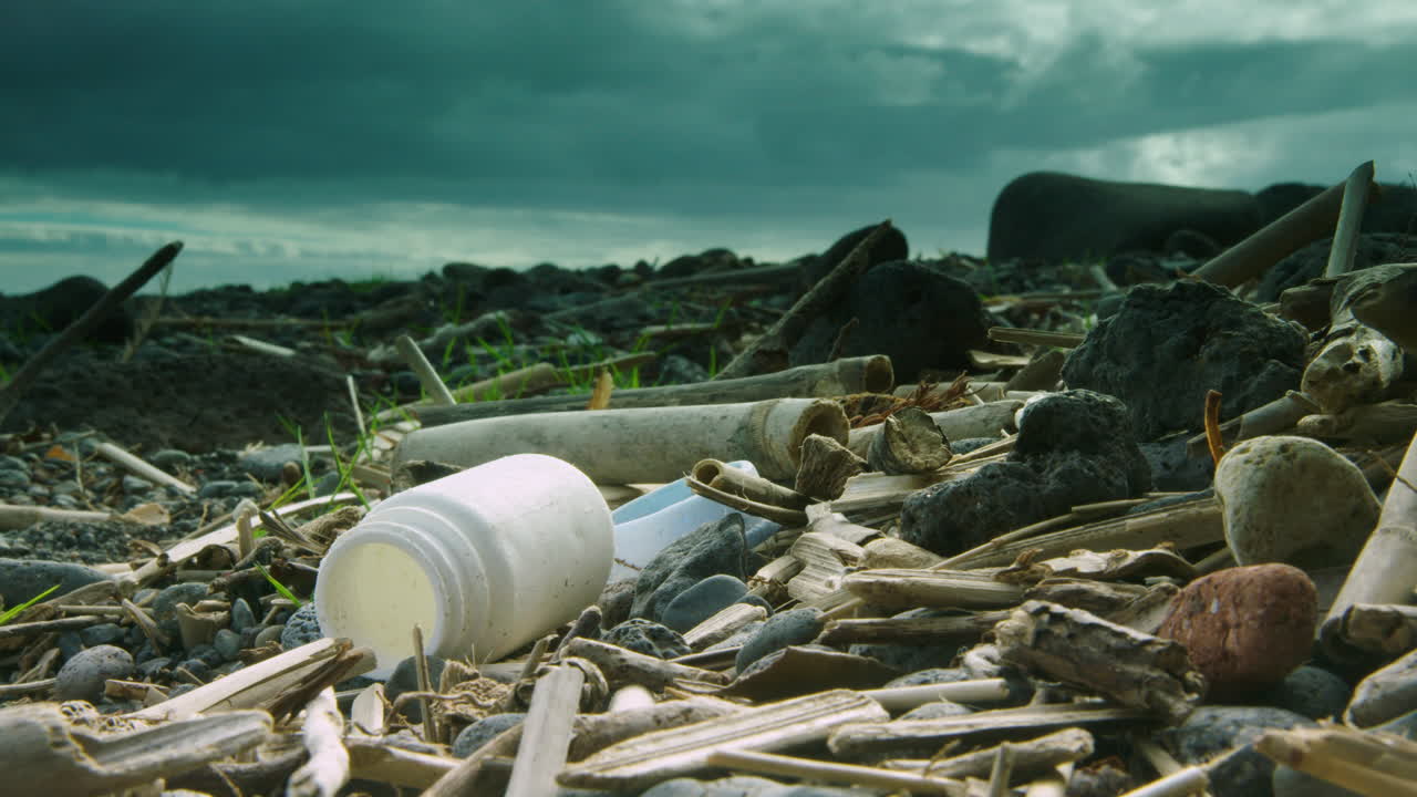 toma profunda de una batalla de plástico lavada en una playa rodeada de otros plásticos y madera a la deriva
