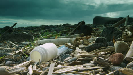 Deep focus shot of a washed up plastic battle lying on a beach surrounded by other plastic and driftwood