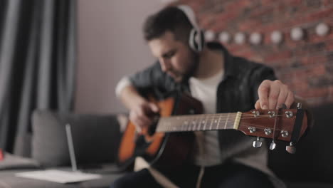 joven músico masculino tocando y ajustando la guitarra en casa