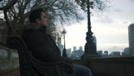 slider shot of man seated on an ornate iron park bench looking at the city
