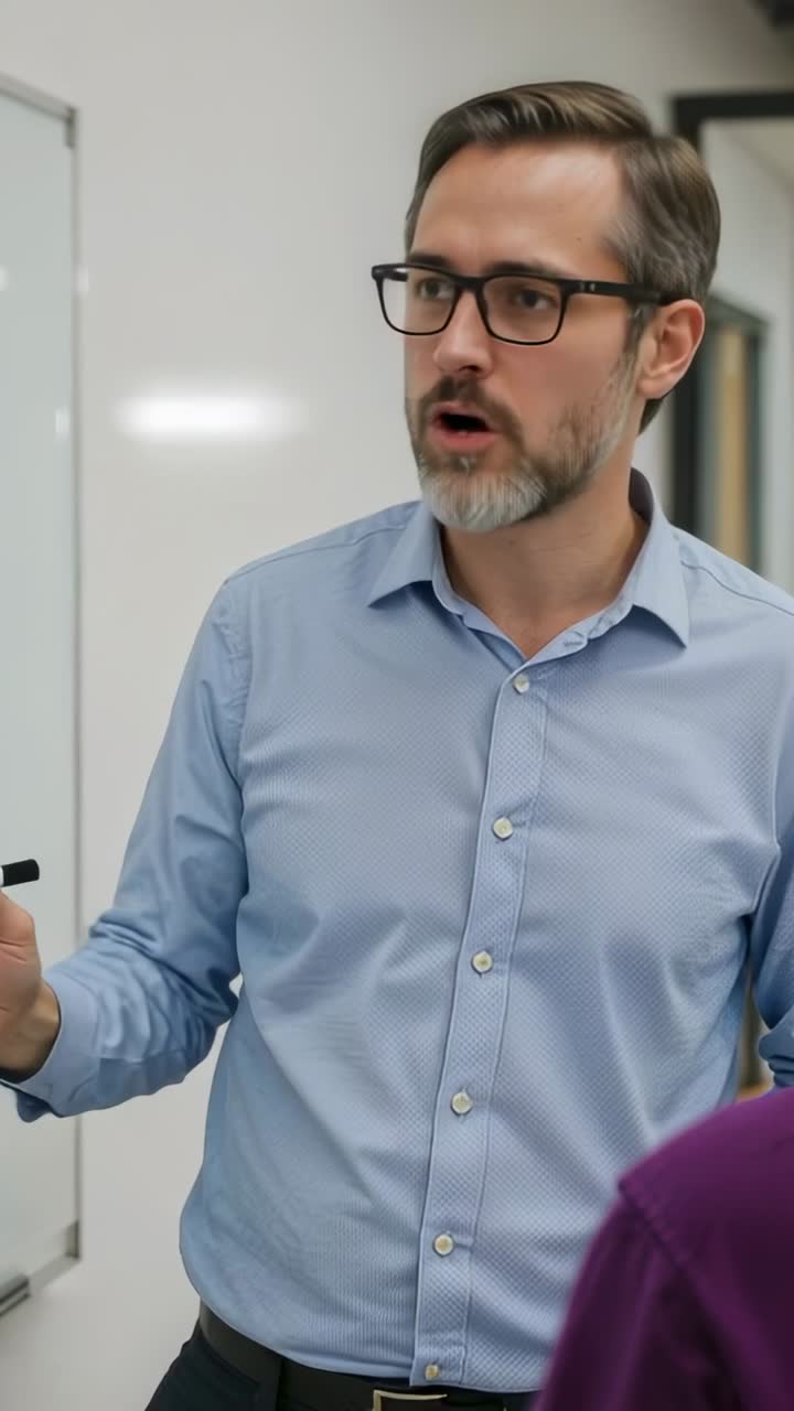 Vertical video: Explaining blue shirt instructor addressing student at whiteboard in boardroom